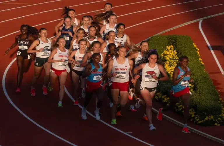 Catholic University in the women’s 5000 meters race into a swath of light in turn three on the final day of NCAA Track and Field Championships at Hayward Field.