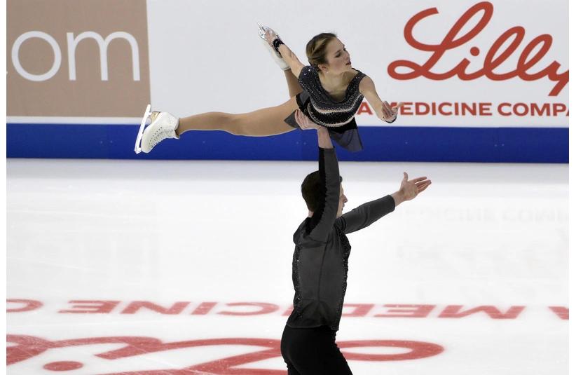 Alisa Efimova and Misha Mitrofanov, a figure skater lifts his partner overhead on the ice, showcasing strength and grace. They wear dark costumes, with logos visible in the background.