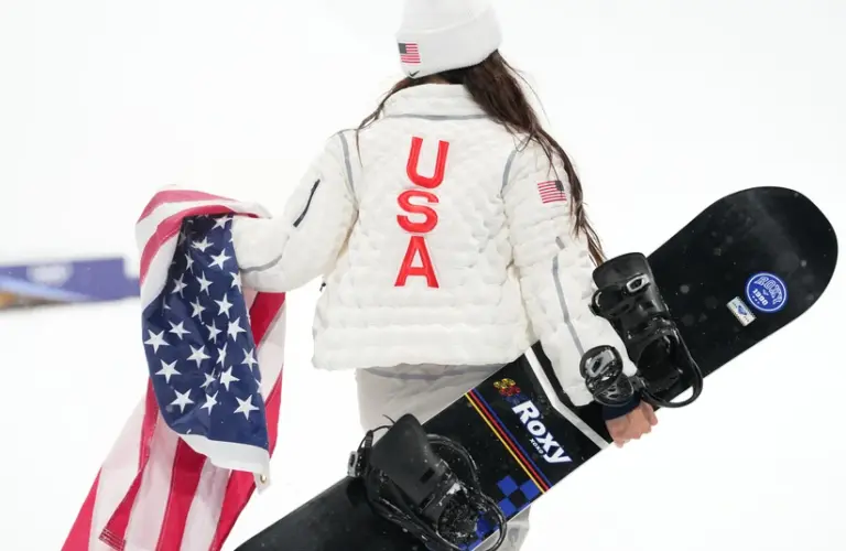 Feb 12, 2026; Livigno, Italy; Chloe Kim of the United States walks with her snowboard and an American flag after the women's halfpipe final during the Milano Cortina 2026 Olympic Winter Games at Livigno Snow Park. Mandatory Credit: Joe Camporeale-Imagn Images
