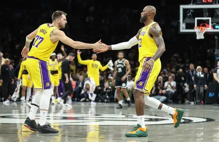 Los Angeles Lakers guard Luka Doncic (77) greets forward LeBron James (23) during a timeout in the first quarter against the Brooklyn Nets