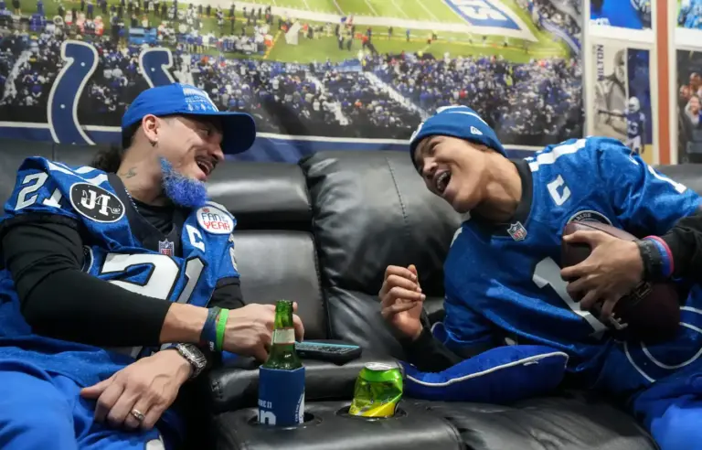 Eli Otero Jr. (left) laughs with his son Eli Otero III as they check their fantasy football league standings on Sunday, Dec. 21, 2025, at their home in Valparaiso, Ind. The entire basement of their home is decorated with various Indianapolis Colts memorabilia collected by the family over the years.